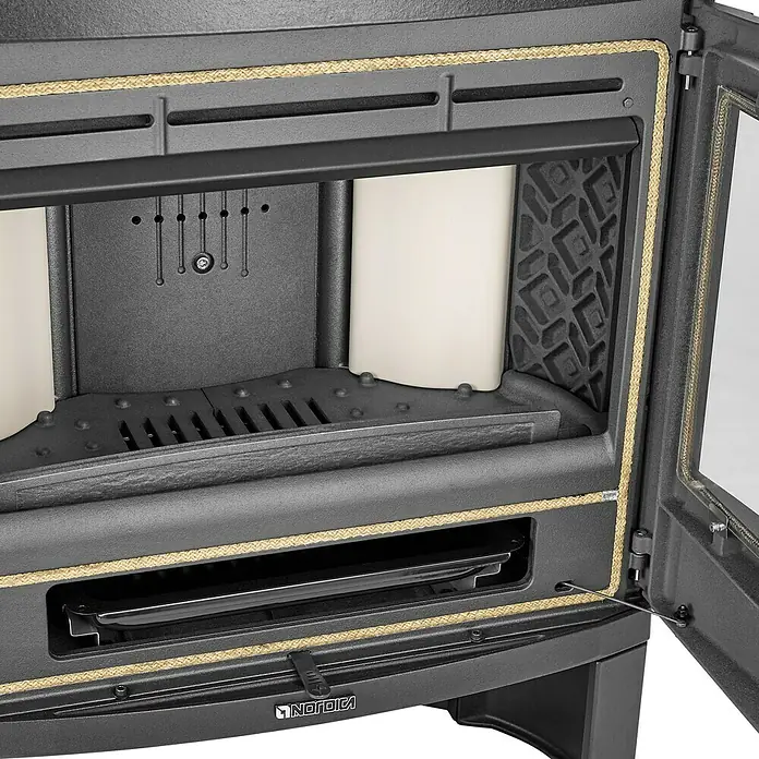 La Nordica Kaminofen Jennifer - 7,5 kW, Raumheizvermögen: 215 m³, Material Verkleidung: Stahl, Schwarz - Nahaufnahme eines Nordica Kaminofens, der Details der Innenarchitektur wie Brennraumauskleidung und Rost zeigt.