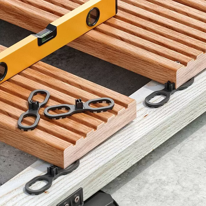 Langfit Abstandhalter - 7 mm, 100 Stk. - Dunkelgraue Terrassenclips befestigen natürliche Holzbretter, ein gelber Wasserwaage sichert die Ausrichtung.