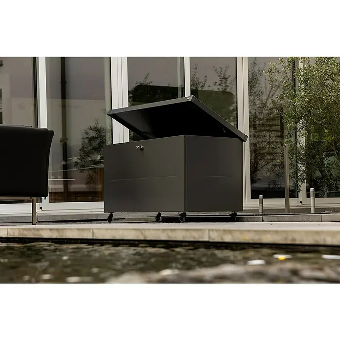 Telluria Gartenbox Nevio 160 - L x B x H: 165 x 85 x 85 cm, Stahl, Anthrazit - Ein grauer, abschließbarer Staukasten mit Rädern steht auf einer Terrasse vor einem Fenster und bietet praktischen Stauraum im Außenbereich.