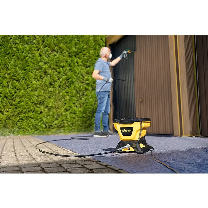 Wagner High Efficiency Airless Farbsprühsystem Control 150 M - 350 W, Förderleistung: 0,9 l/min - Mann lackiert Garagentor mit Wagner Farbsprühsystem. Das gelb-schwarze Farbsprühgerät steht im Vordergrund.