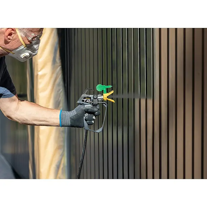 Wagner High Efficiency Airless Farbsprühsystem Control 150 M - 350 W, Förderleistung: 0,9 l/min - Nahaufnahme eines Mannes mit einer Wagner T2 Farbspritzpistole, der einen Zaun streicht. Das Werkzeug sorgt für einen gleichmäßigen Farbauftrag.