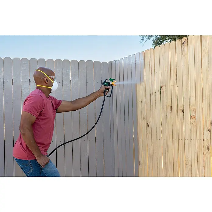 Wagner High Efficiency Airless Farbsprühsystem Control 150 M - 350 W, Förderleistung: 0,9 l/min - Ein Mann sprüht mit einer Farbpistole Farbe auf einen Holzzaun, um diesen zu renovieren. Er trägt dabei Schutzkleidung.