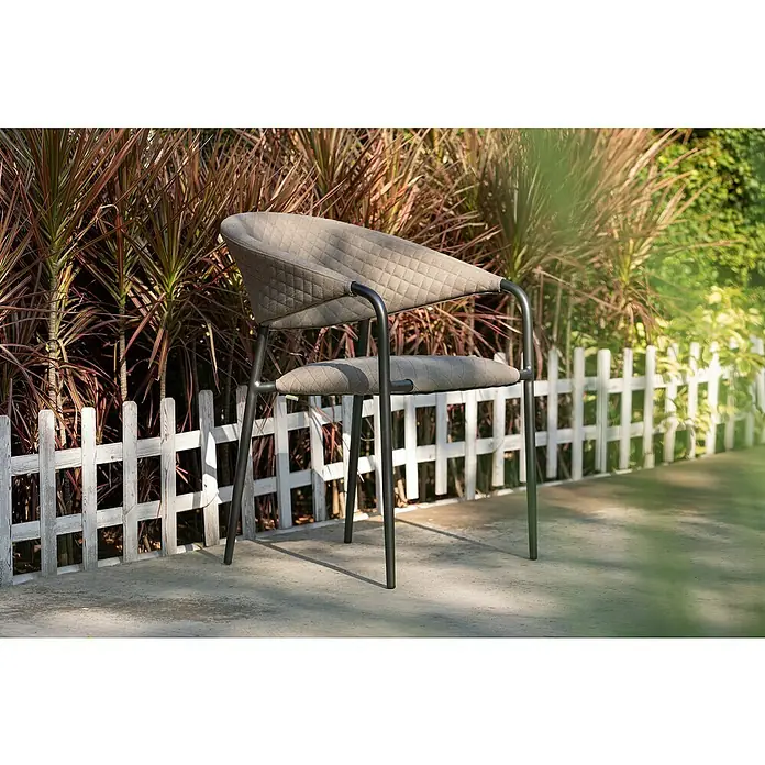 Stapelsessel - Stapelbar, Beige, B x T x H: 64,8 x 59,7 x 83 cm - Elegantes Gartenmöbel: Ein moderner, gesteppter Sessel mit dunklem Gestell steht vor einem weißen Zaun, umgeben von üppigem Grün.