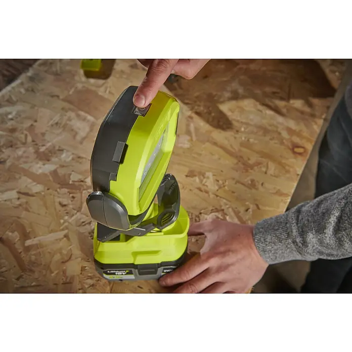 Ryobi ONE+ LED-Akkustrahler RLCL18-0 - 18 V, Ohne Akku, 800 lm - Nahaufnahme einer Person, die eine grüne Akku-Arbeitsleuchte auf einer Holzoberfläche einschaltet.