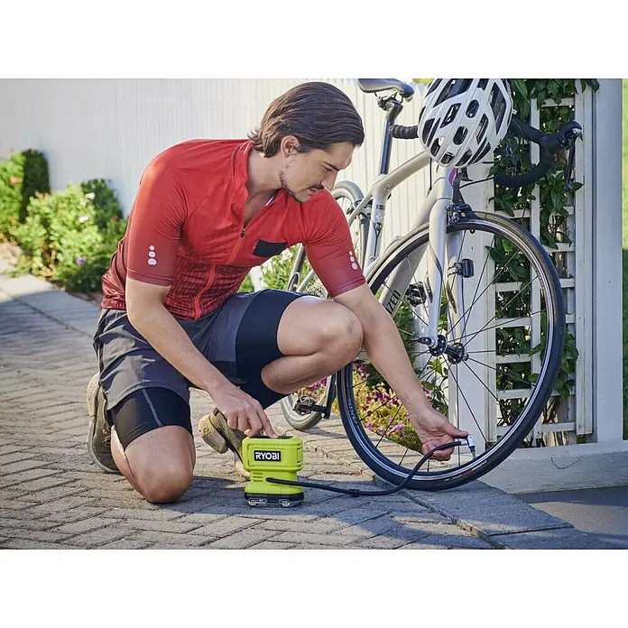 Ryobi ONE+ Akku-Kompressor RPI18-0 - 18 V, Ohne Akku, 10,3 bar - Ein Mann kniet neben einem Fahrrad und benutzt eine gelbe RYOBI Luftpumpe, um den Reifen aufzupumpen.