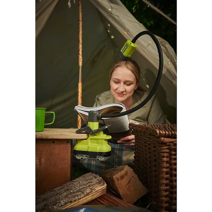Ryobi ONE+ LED-Akkustrahler RLCF18-0 - 400 lm - Eine Frau liest in einem Zelt mit einer RYOBI ONE+ Lampe, die auf einem Holztisch befestigt ist und Licht spendet.