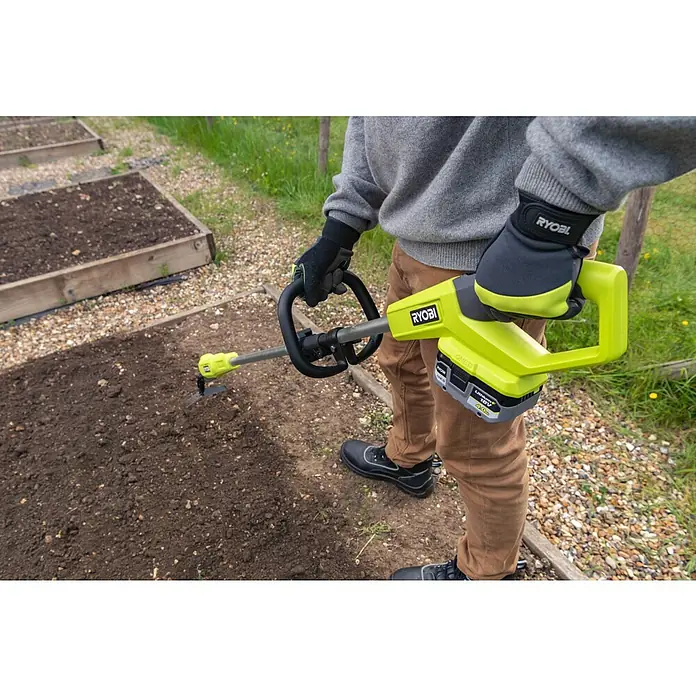 Ryobi ONE+ Akku-Bodenhacke RY18GHA - 18 V, Anzahl Akkus: Ohne Akku, Li-Ionen - Nahaufnahme eines Gärtners, der mit einem gelben RYOBI Akku-Kultivator arbeitet, um den Boden in einem Gartenbeet aufzulockern.