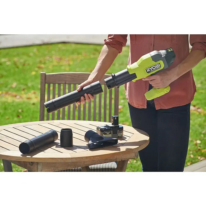 Ryobi ONE+ Akku-Laubbläser RY18BLCXA-0 - 18 V, Ohne Akku, Blasgeschwindigkeit: 241,4 km/h, Blasleistung: 6,51 m³/min - Eine Person montiert einen Ryobi Akku-Laubbläser mit verschiedenen Aufsätzen auf einem Holztisch im Freien.