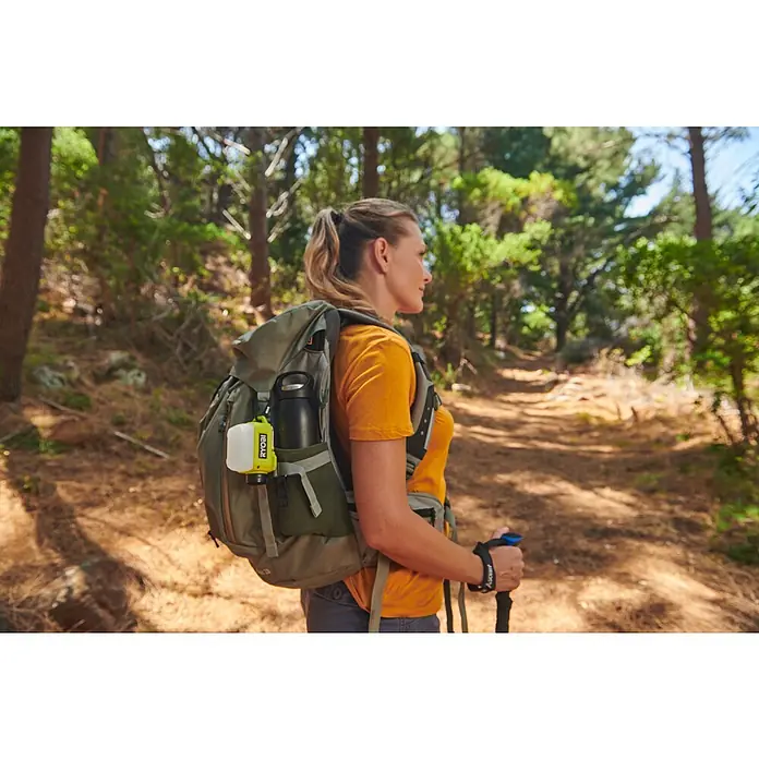 Ryobi 4V USB LED-Akkustrahler RLA4-0 - 300 lm - Frau wandert mit einem Rucksack, an dem eine RYOBI-Laterne befestigt ist, durch den Wald. Die RYOBI-Laterne bietet Licht beim Wandern.