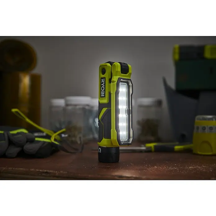 Ryobi 4V USB Akku-Stableuchte RLI4-120G - 4 V, 1 Akku, 2 Ah - Nahaufnahme einer leuchtenden, gelb-schwarzen Ryobi Arbeitsleuchte auf einer Werkbank.