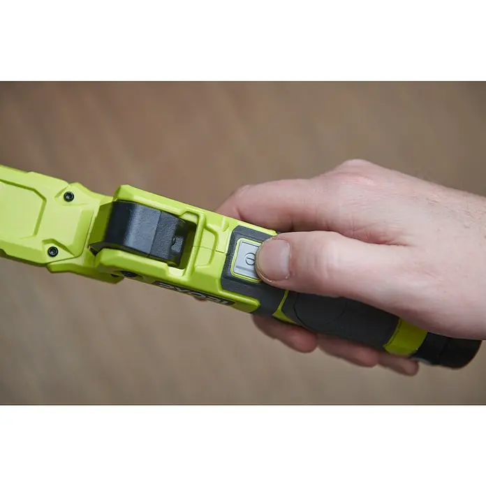 Ryobi 4V USB Akku-Stableuchte RLI4-120G - 4 V, 1 Akku, 2 Ah - Nahaufnahme eines Ryobi-Werkzeugs mit einer Hand, die den Netzschalter drückt, der sich auf einem gelb-grauen Gehäuse befindet.