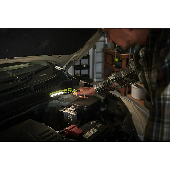 Ryobi 4V USB Akku-Stableuchte RLI4-120G - 4 V, 1 Akku, 2 Ah - Ein Mann, der mit einer Ryobi-Arbeitsleuchte unter der Motorhaube eines Autos arbeitet. Die LED Lampe beleuchtet den Motorraum.