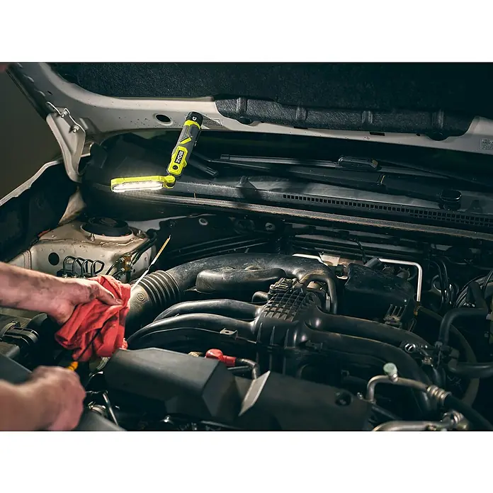 Ryobi 4V USB Akku-Stableuchte RLI4-120G - 4 V, 1 Akku, 2 Ah - Der Ryobi-Arbeitsstrahler leuchtet einen Automotor aus, der von einer Person mit einem roten Tuch gewartet wird.