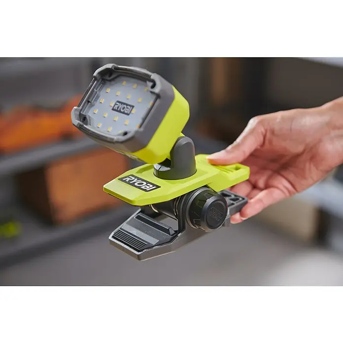 Ryobi 4V USB LED-Akkustrahler RLC4-0 - 1.000 lm - Ein Ryobi LED-Arbeitslicht mit Klemme wird von einer Hand gehalten. Das Licht ist grün und grau und hat ein verstellbares Design.