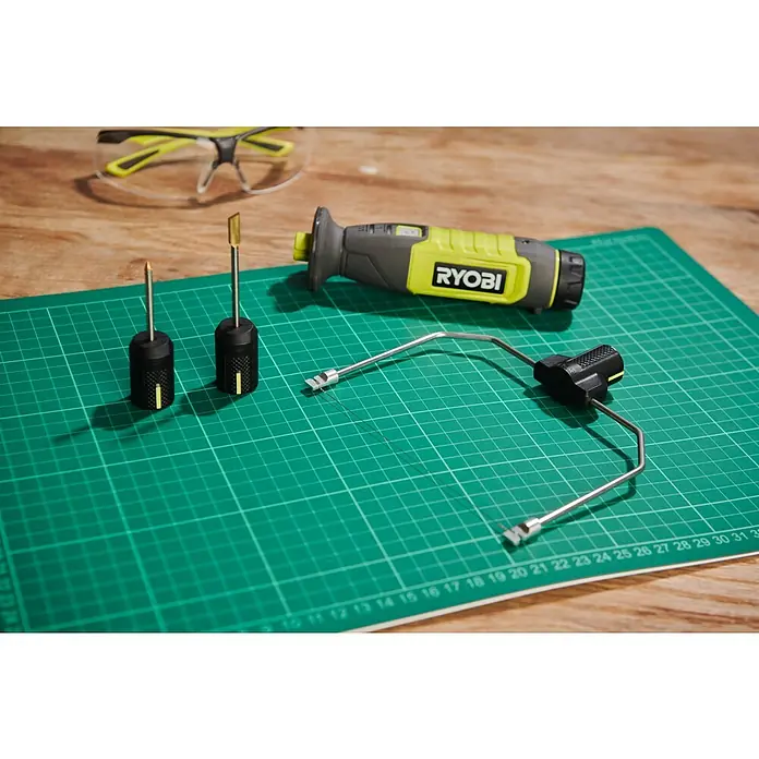 Ryobi 4V USB Akku-Heißdrahtschneider RHC4 - 4 V, Ohne Akku - Ein Ryobi-Werkzeug-Set mit Schleifaufsätzen, Schneideaufsatz und Sicherheitsbrille auf einer grünen Schneidematte.