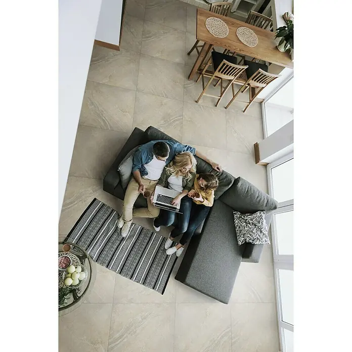Feinsteinzeugfliese Geostone - 80 x 80 cm, Braun, Glänzend - Eine Familie sitzt auf einer grauen Couch und benutzt einen Laptop, während sie sich entspannt. Der Raum ist hell und modern mit Fliesenboden.