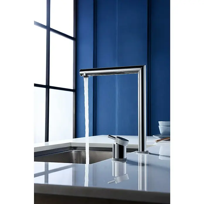 Imex Grifo de cocina escamoteable Itaca - Cromo - Primer plano de un grifo cromado moderno y elegante que dispensa agua limpia en un fregadero de acero inoxidable, con un fondo azul.