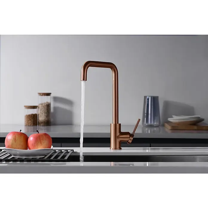Imex Grifo de cocina Loira - Oro rosa - Un moderno grifo de cobre con agua corriente en una cocina elegante, complementado con manzanas frescas y elegantes tarros de almacenamiento.