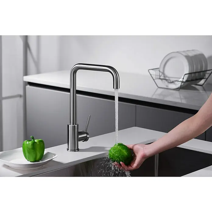 Imex Grifo de cocina Loira - Black gun metal - Moderno grifo de cocina de acero inoxidable. Una mano sostiene un pimiento verde bajo el agua corriente del grifo.