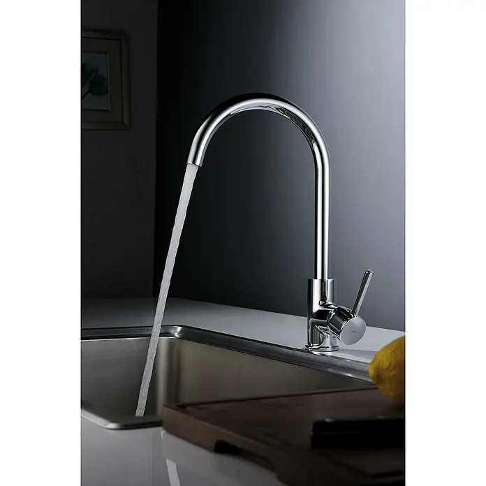 Imex Grifo de cocina Lyon - Cromo - Un moderno grifo de cocina cromado está en uso, el agua fluye hacia un fregadero de acero inoxidable, con un limón cerca.
