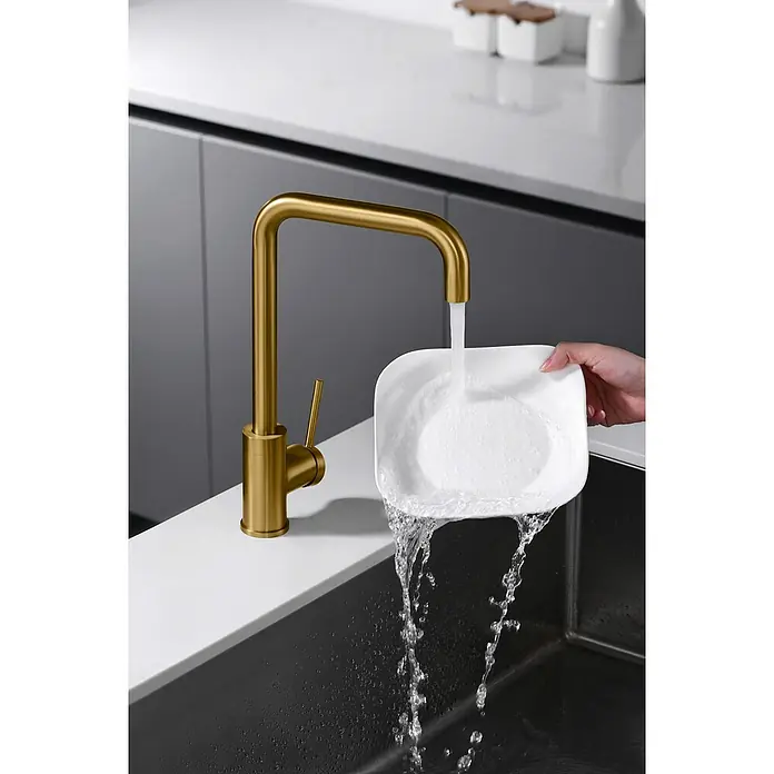 Imex Grifo de cocina Loira - Oro - Grifo dorado moderno en un entorno de cocina con plato bajo el agua corriente.