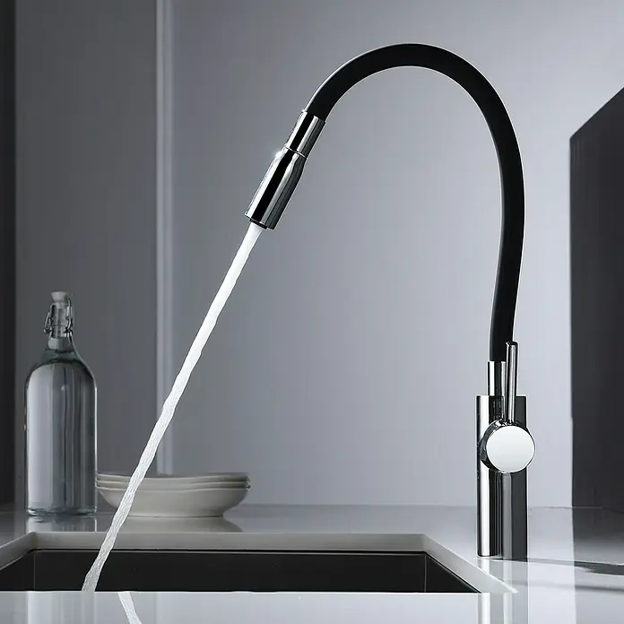 Imex Grifo de cocina flexible Tokyo - Negro/Cromo, Brillante - Moderno grifo de cocina negro con rociador extraíble vertiendo agua. El grifo destaca sobre un fondo de cocina luminoso.
