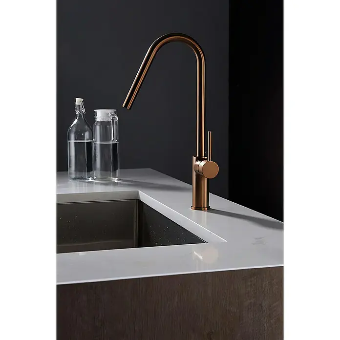 Imex Grifo de cocina Kenia - Oro rosa - Primer plano de un elegante grifo de color bronce junto a un fregadero y botellas de vidrio, destacando el diseño moderno y los accesorios de cocina de calidad.