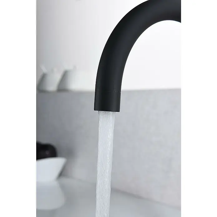 Imex Grifo de cocina Manacor - Negro - Primer plano de un moderno grifo negro mate con un fuerte chorro de agua que fluye de él, sobre un fondo neutro.