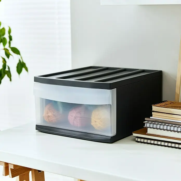 Rotho Schubladenbox Systemix L - L x B x H: 39,5 x 34 x 20,3 cm, Anthrazit, Anzahl Schubladen: 1 Stk. - Das Bild zeigt eine graue Aufbewahrungsbox mit einer transparenten Schublade, die mit bunten Wollknäueln gefüllt ist, auf einem weißen Tisch.