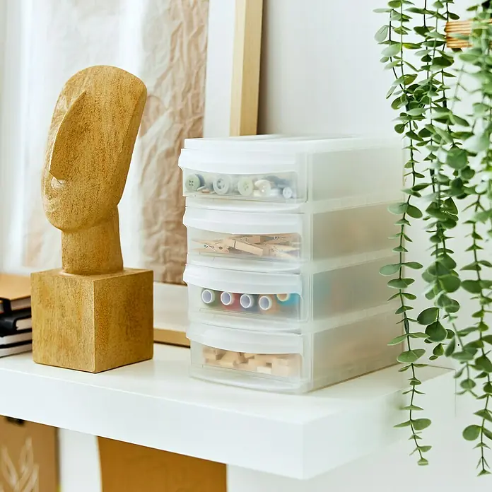 Rotho Schubladenbox Systemix XS - L x B x H: 19,6 x 4,2 x 23,3 cm, Transparent, Anzahl Schubladen: 4 Stk. - Ein durchsichtiges Schubladen-Set mit vier Fächern, gefüllt mit verschiedenen Bastelutensilien, steht auf einem weißen Regal neben Dekoration.