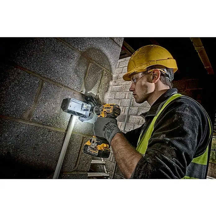DeWalt XR 18V Taladro atornillador percutor de batería DCD796P2 -  - Un trabajador de la construcción fija una caja de conexiones a una pared de ladrillo con un taladro inalámbrico amarillo DeWalt. Lleva ropa protectora.
