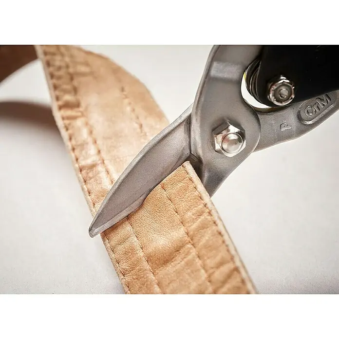 Stanley FatMax Blechschere - Länge: 250 mm, Schnittlänge: 1,2 mm, Gerade - Nahaufnahme einer Blechschere, die einen hellbraunen Ledergürtel schneidet, wobei die Details der Werkzeugklinge und des Gürtelmaterials hervorgehoben werden.