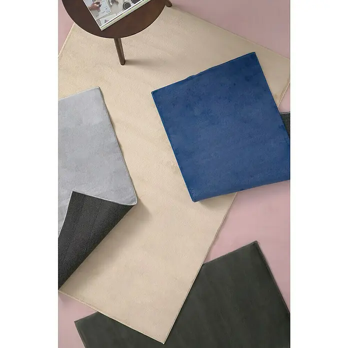 Alfombra de pelo corto Aiden - Kaki, 110 x 60 cm, Poliéster - Primer plano de varias alfombras cuadradas de colores sobre un fondo rosa claro, incluyendo una mesa redonda.