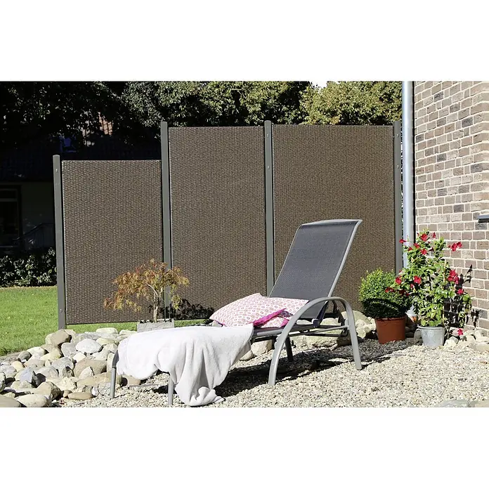 Sichtschutzelement Stockholm - 90 x 150 cm, Dunkelbraun - Ein gemütlicher Gartenbereich mit einer grauen Sonnenliege, einem dekorativen Sichtschutzzaun und blühenden Pflanzen.
