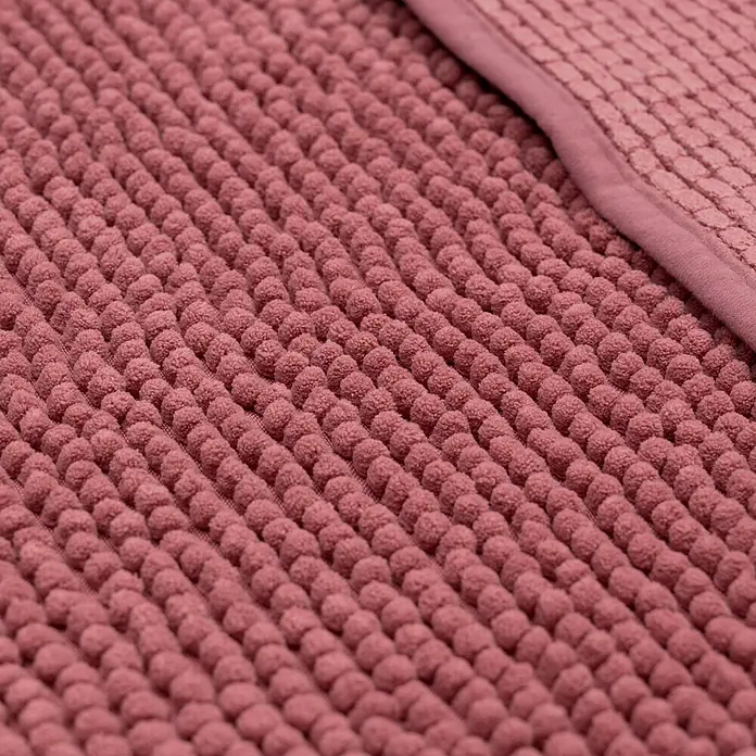 Camargue Badteppich Zottel - 50 x 80 cm, Brombeere, 100% Polyester - Nahaufnahme eines rosafarbenen Badteppichs mit Noppenstruktur und einem Rand aus glattem Stoff für ein weiches und dekoratives Badezimmerambiente.