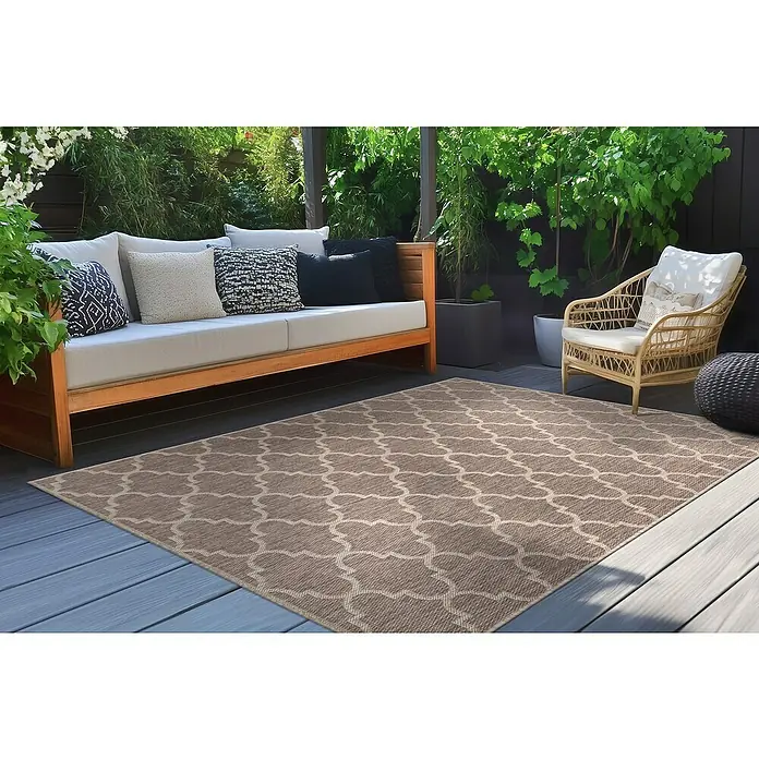 Outdoor-Teppich Casa - Taupe, 150 x 80 cm, 100 % Polypropylen - Outdoor-Szene mit beigem Teppich mit marokkanischem Muster, passend zu den Gartenmöbeln und der üppigen Vegetation im Hintergrund.