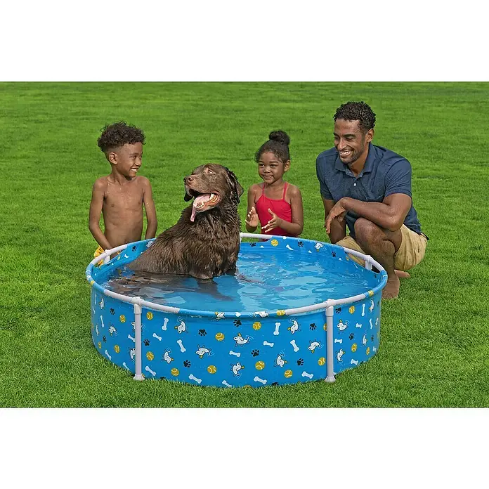 Bestway Frame-Pool Pfote für Haustiere - Ø x H: 122 cm x 30,5 mm, Blau, 292 l - Ein Hund genießt ein erfrischendes Bad in einem blauen Planschbecken mit Hunde-, Knochen- und Ballmotiven, während Kinder und ein Mann zusehen.