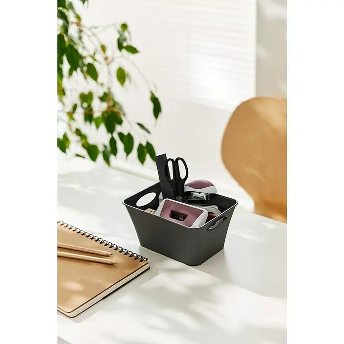 Rotho Aufbewahrungsbox Living - L x B x H: 18 x 13,4 x 9 cm, Kunststoff, Anthrazit - Ein grauer Organizer-Korb mit Büromaterialien steht auf einem Schreibtisch, neben einem Notizbuch und zwei Stiften.
