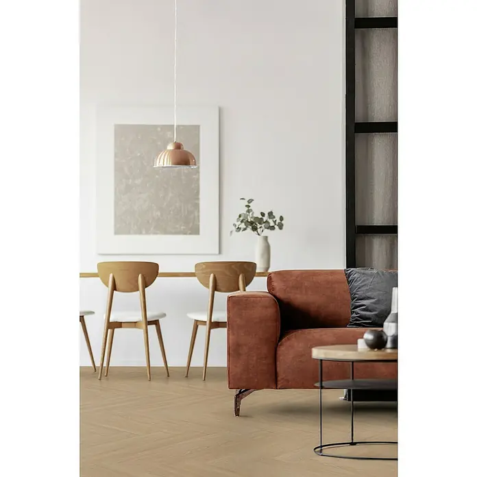 Gerflor Vinylboden Rigid Acoustic - Tulum Natural, Fischgrät, 750 x 125 x 6 mm - Ein helles Wohnzimmer mit einem braunen Sofa, Holzböden im Fischgrätmuster und passenden Holzstühlen mit weißer Sitzfläche.