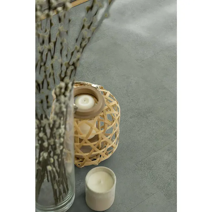 Gerflor Vinylbodenmuster Rigid Acoustic Oliva Green - 250 x 399 x 5,4 mm, Oliva Green - Nahaufnahme von Deko-Kerzen und einer Vase mit Zweigen auf einem grauen Boden. Die Kerzen spenden warmes Licht.