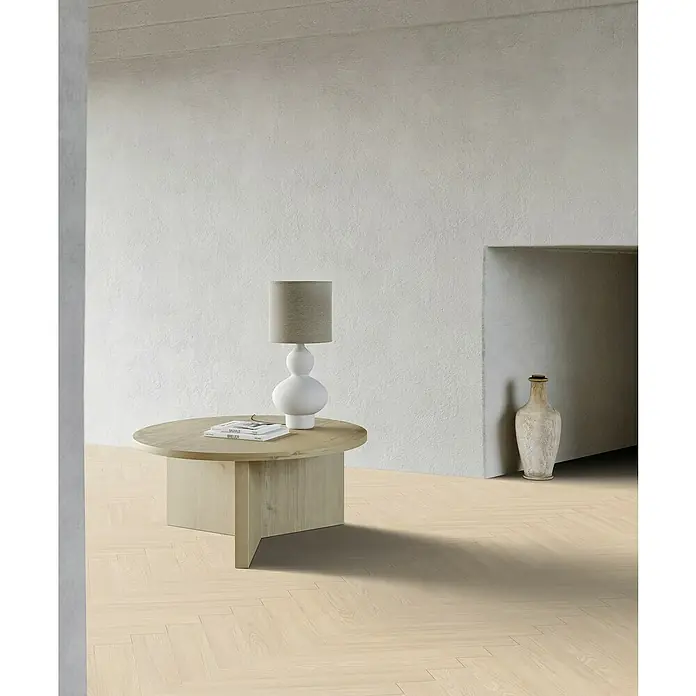 Gerflor Vinylboden Rigid Acoustic - Tulum Cream, Fischgrät, 750 x 125 x 6 mm - Einrichtungsidee mit einem runden Couchtisch aus hellem Holz, einer Lampe und einer Vase, die ein gemütliches Ambiente schaffen.