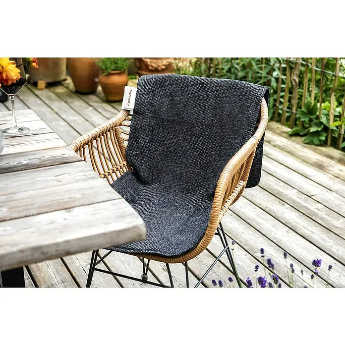 Montandor Heizdecke - 145 x 48 cm, Dunkelgrau - Nahaufnahme eines Korbstuhls mit einer anthrazitfarbenen Sitzauflage auf einer Holzterrasse, neben einem Tisch mit einem Weinglas.
