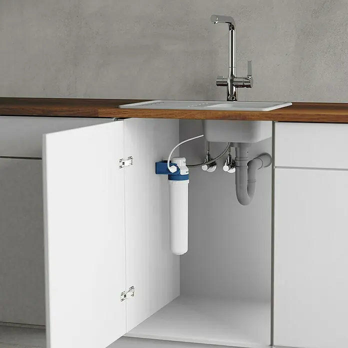 BWT Wasserfilter Blueperl - Passend für: Spültischarmatur Blueperl - Untertisch-Wasserfilter unter einer Spüle in einem Küchenschrank. Das Gerät ist blau-weiß und hängt an der Schrankwand.