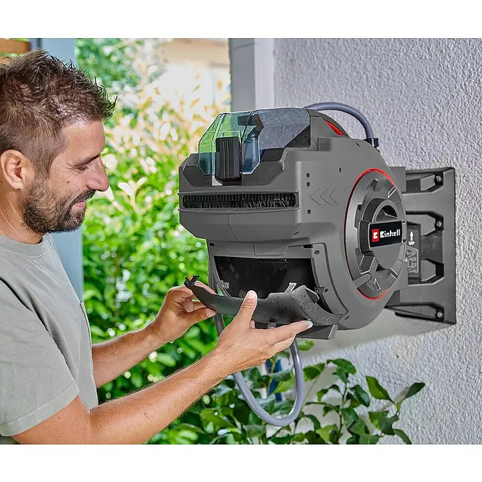 Einhell Power X-Change 18V Akku-Schlauchtrommel GE-HR 18/30 WH Li-Solo - 18 V, Ohne Akku - Mann inspiziert eine Einhell Schlauchbox an einer Wand. Die Box ist grau mit roten Akzenten und einem durchsichtigen Deckel.