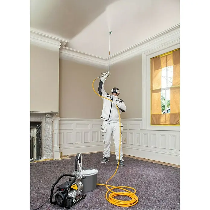Wagner High Efficiency Airless Farbsprühsystem SuperFinish 21 Pro HEA - 900 W, Förderleistung: 2,1 l/min - Ein Maler streicht eine Zimmerdecke mit einem Wagner Airless Farbspritzgerät. Die Maschine steht auf dem Boden und ist über einen Schlauch verbunden.