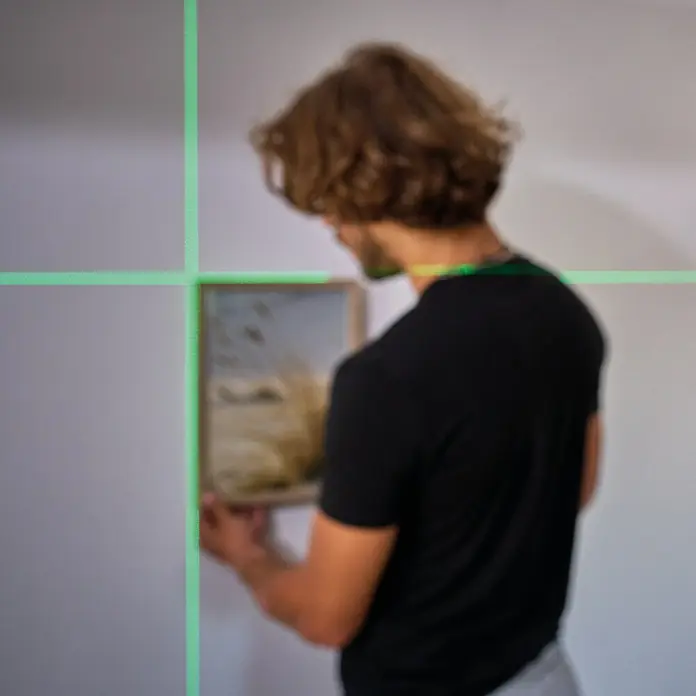 Einhell Kreuzlinienlaser TC-LL 2 G - Max. Arbeitsbereich: 0 m - 16 m - Mann hängt mit einem Laserpointer ein gerahmtes Bild an einer weißen Wand auf.