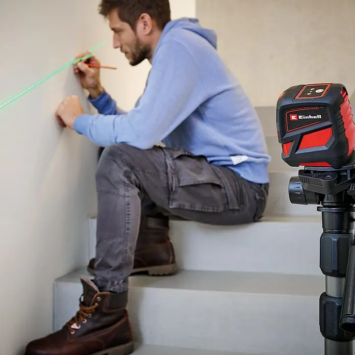 Einhell Kreuzlinienlaser TC-LL 2 G - Max. Arbeitsbereich: 0 m - 16 m - Mann benutzt Einhell Kreuzlinienlaser zum Markieren an einer Wand. Der Laser ist rot und schwarz und steht auf einem Stativ.