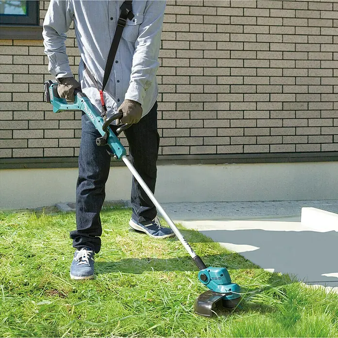 Makita LXT 18V Akku-Rasentrimmer DUR193F01 - 18 V, Li-Ionen, 1 Akku - Ein Mann benutzt einen Makita Akku-Rasentrimmer, um seinen Rasen zu pflegen. Der Trimmer ist blaugrün und hat einen verstellbaren Griff.