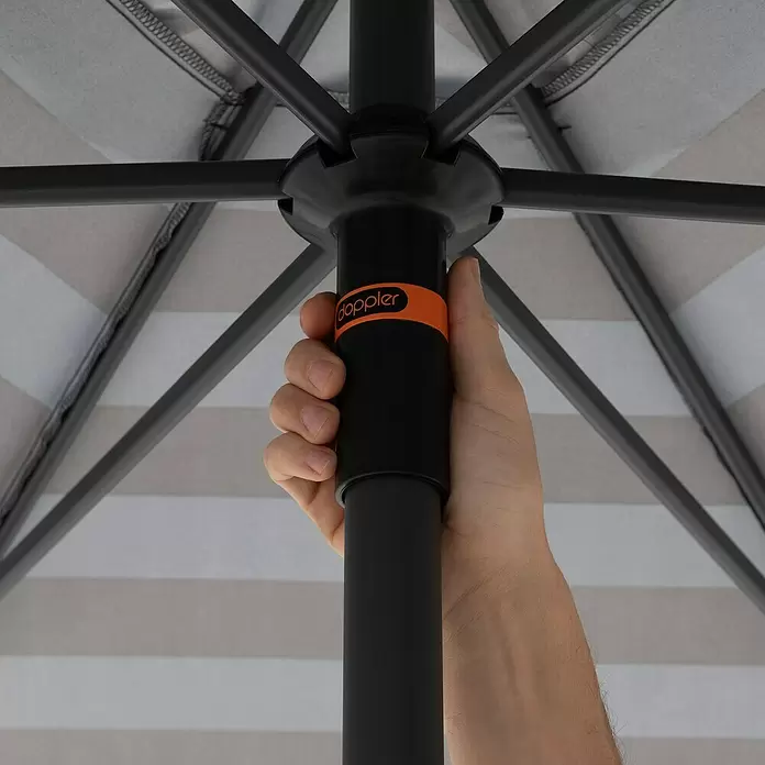 Doppler Marktschirm myZone Push Up - Blockstreifen Anthrazit, Durchmesser Bespannung: 300 cm - Hand hält schwarzen Regenschirmstock mit orangefarbenem 'doppler'-Logo. Gestreiftes hellgrau-beiges Dach sichtbar.