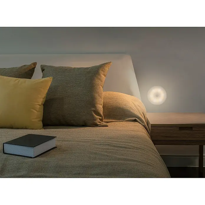 Tween Light Akku-Unterbauleuchte - Weiß, Mehrfarbig - Dieses Bild zeigt eine runde LED-Nachtleuchte an einer Wand neben einem Bett, die für sanftes Licht im Schlafzimmer sorgt.